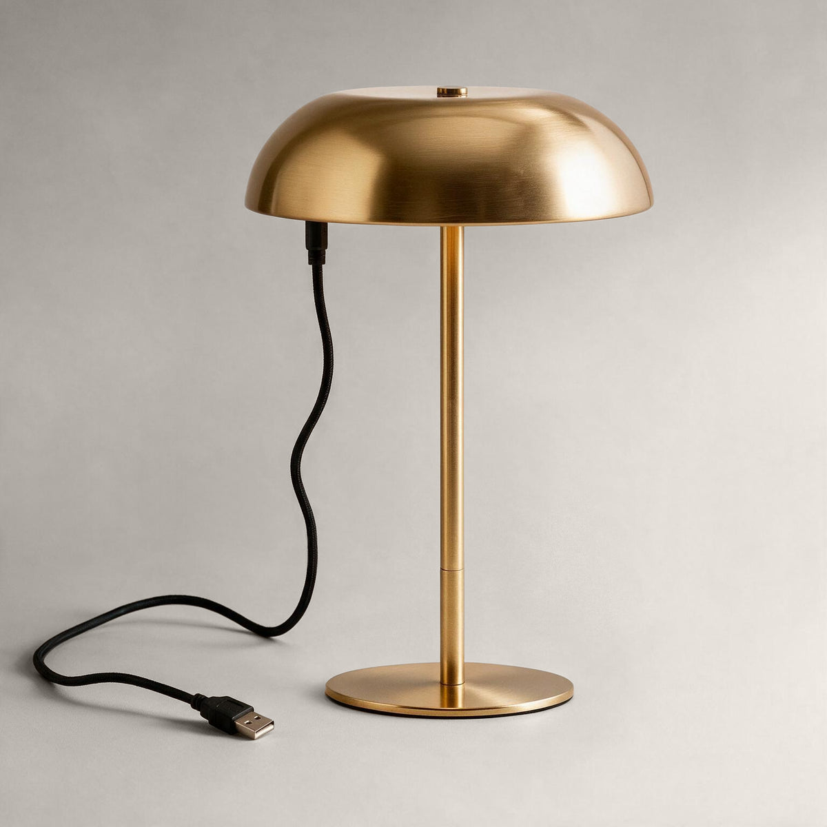 Brushed brass cordless mushroom table lamp connected to a USB charging cable