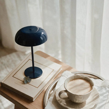 Glossy navy cordless mushroom table lamp styled on books beside a cup of coffee.