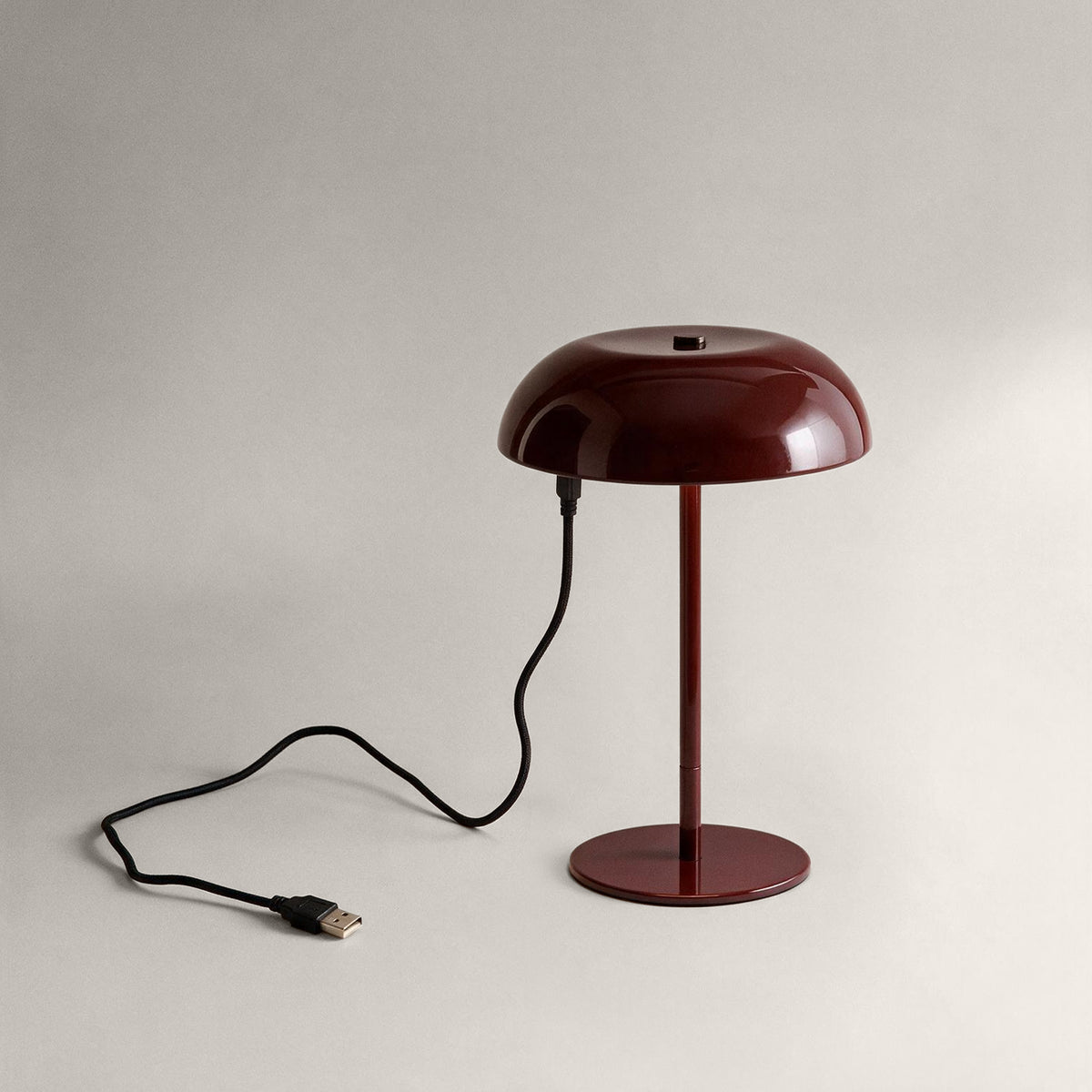 Oxblood cordless mushroom table lamp connected to a USB charging cable