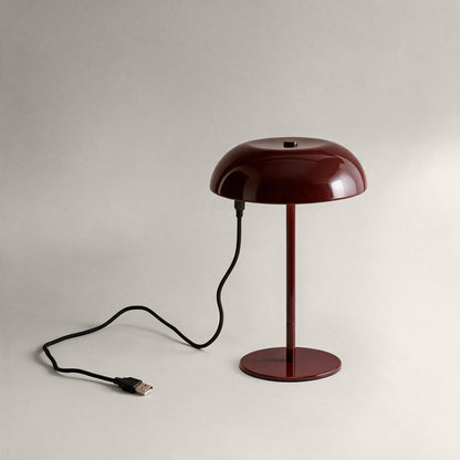 Oxblood cordless mushroom table lamp connected to a USB charging cable