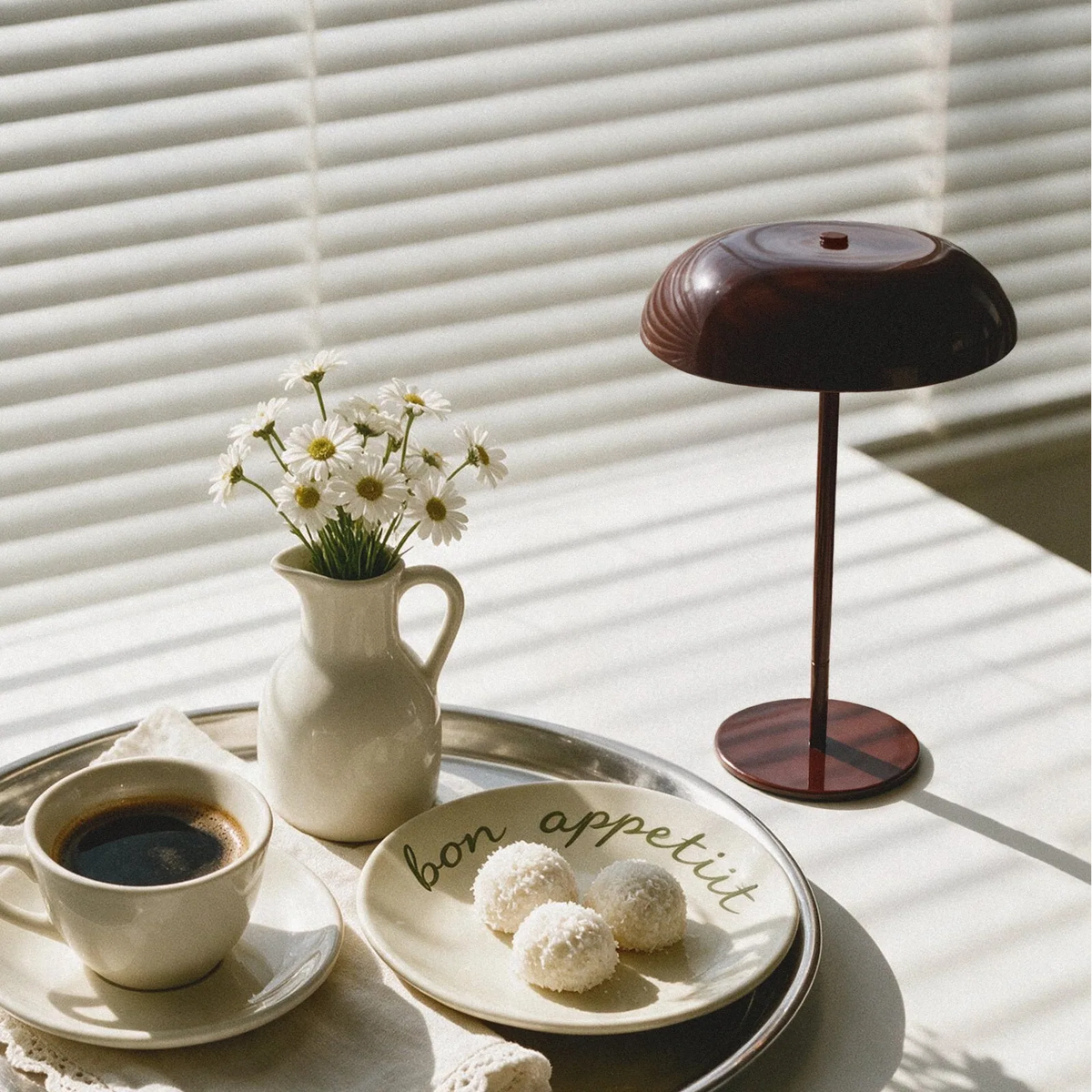 Glossy oxblood cordless mushroom table lamp on a sunlit table with coffee and flowers.