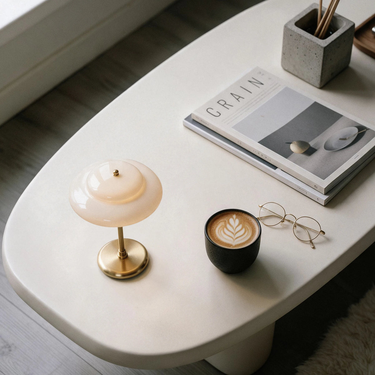 Lampworks opal glass table lamp on a white coffee table beside a latte, eyeglasses and books