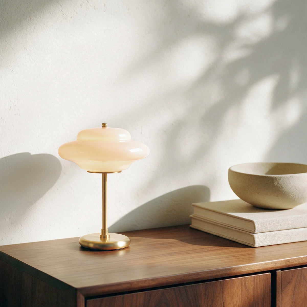 Lit Lampworks glass table lamp on a wood sideboard beside stacked books and a ceramic bowl