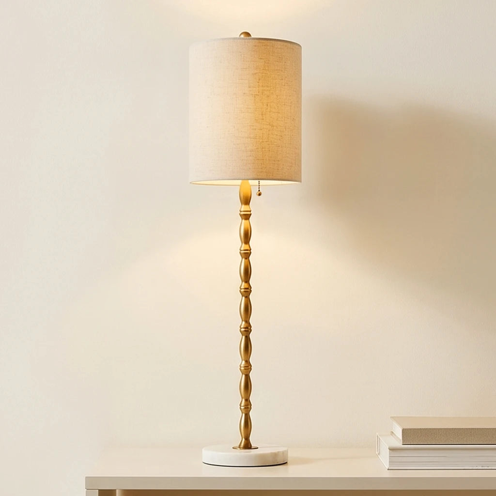 Single Noor brass-finish buffet lamp with a white marble base and linen drum shade on a console.